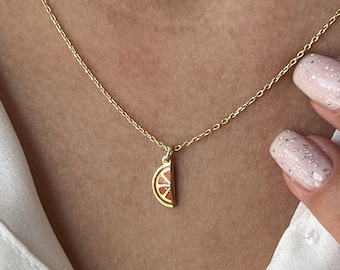 May include: A gold chain necklace with a small orange slice pendant. The pendant is detailed with a white center and a gold outline.