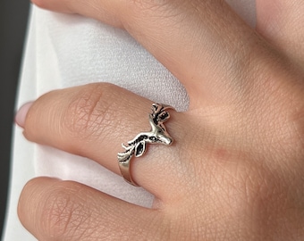 May include: A silver ring featuring a detailed deer head design. The ring is worn on a finger.