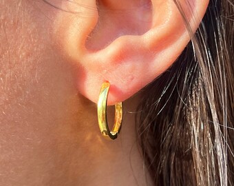 May include: A close-up of a person's ear with a gold hoop earring. The earring is simple and elegant, with a smooth, polished finish.