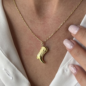 Pode incluir: Um colar de corrente de ouro com um pingente de ouro detalhado em forma de garra.
