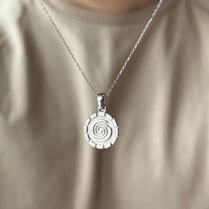 May include: A silver chain necklace with a circular pendant featuring a spiral design.