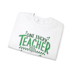 Puede incluir: Camiseta blanca con un tr&eacute;bol verde y el texto "ONE LUCKY TEACHER" en verde.