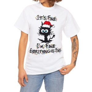 May include: White t-shirt with a black cat wearing a Santa hat and surrounded by Christmas lights. The text "It's Fine I'm Fine Everything is Fine" is written in black.