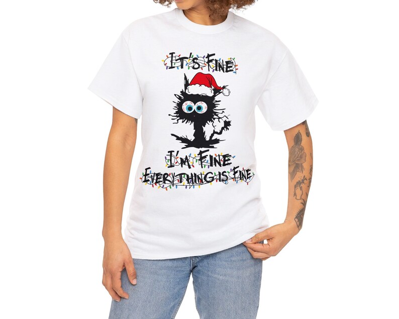 May include: White t-shirt with a black cat wearing a Santa hat and surrounded by Christmas lights. The text "It's Fine I'm Fine Everything is Fine" is written in black.