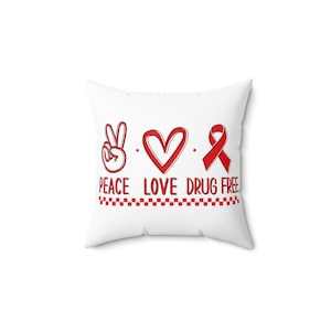 May include: White pillow with red peace sign, heart, and ribbon with the text "Peace Love Drug Free" and a red and white checkered line.