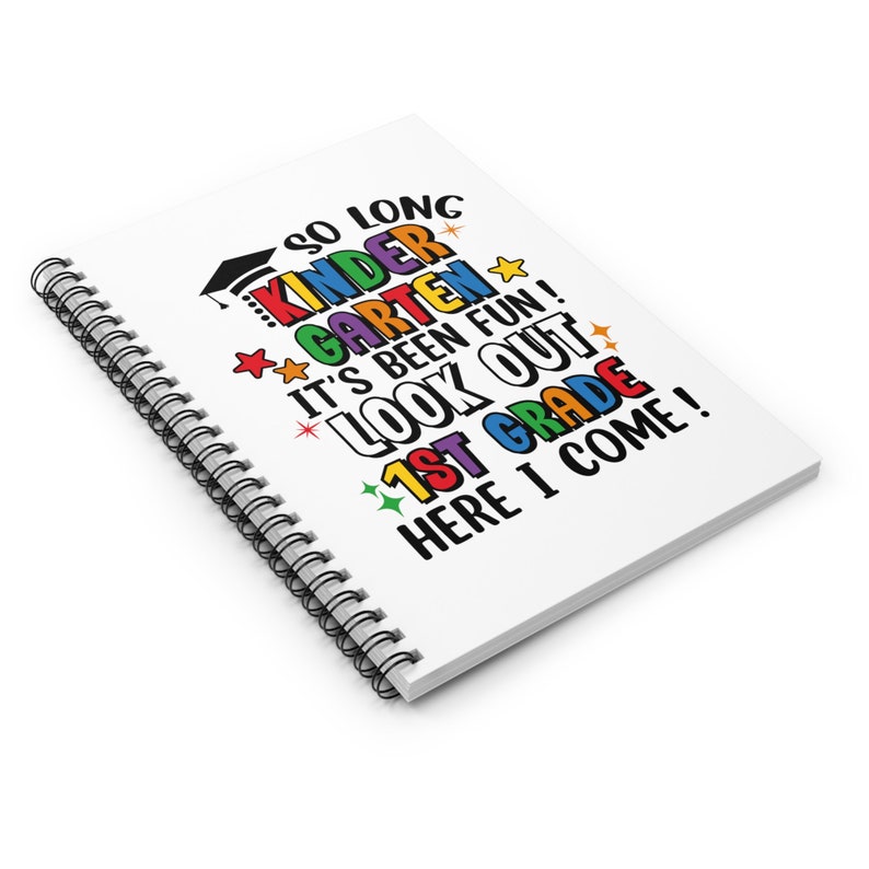 May include: A white spiral notebook with the text "SO LONG KINDER GARDEN IT'S BEEN FUN! LOOK OUT 1ST GRADE HERE I COME!" in colorful letters. The text is decorated with stars and a graduation cap.