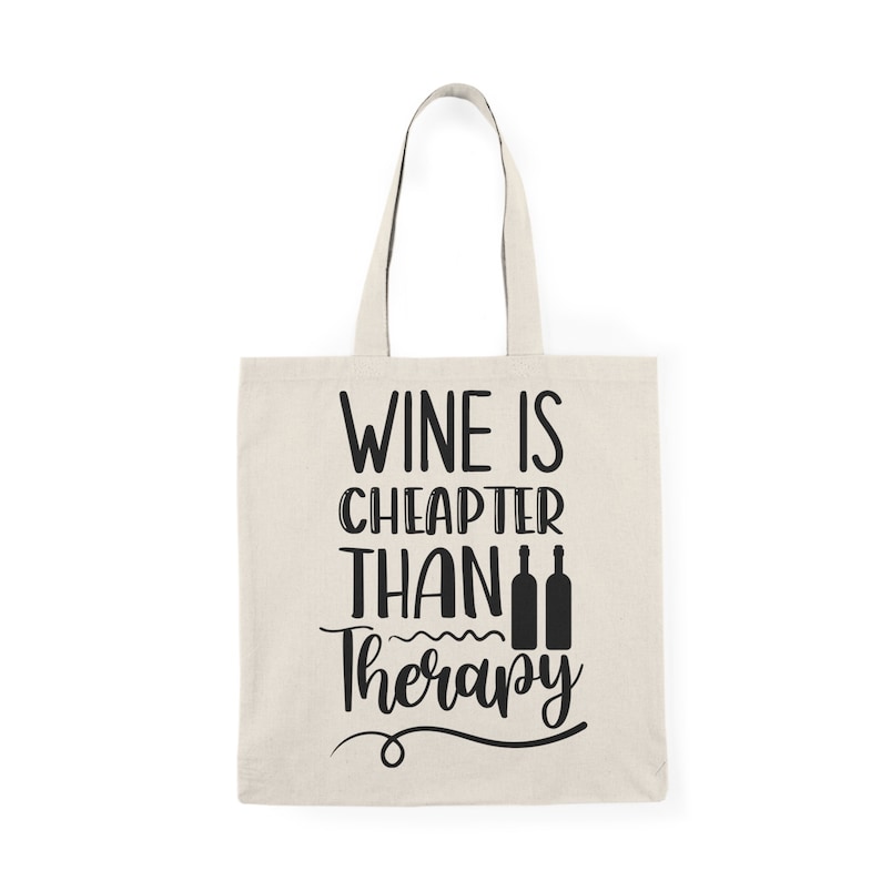 May include: A white canvas tote bag with black text that reads "Wine is cheaper than therapy" with three wine bottle silhouettes.