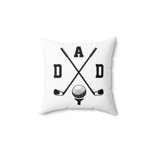 May include: White square throw pillow with a black graphic design. The design features the word "DAD" with golf clubs crossed in the center, and a golf ball on a tee. The pillow is a decorative item.