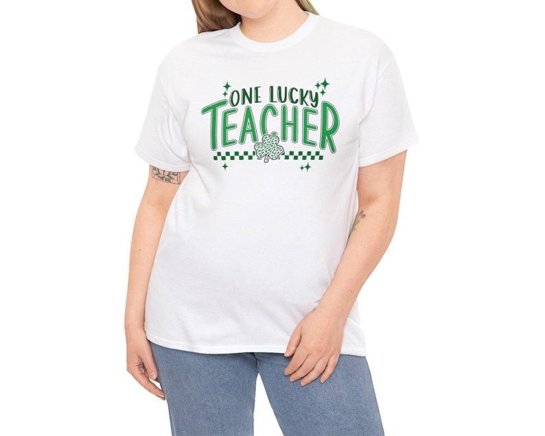 Puede incluir: Camiseta blanca con texto verde que dice "One Lucky Teacher" y un tr&eacute;bol verde.