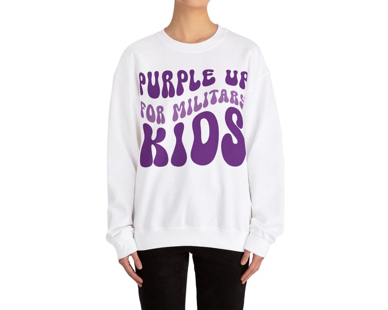 Puede incluir: Sudadera blanca con un gr&aacute;fico morado que dice "Purple Up For Military Kids" en una fuente retro.