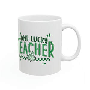 Puede incluir: Taza de cer&aacute;mica blanca con un tr&eacute;bol verde y el texto "One Lucky Teacher" en letras verdes.