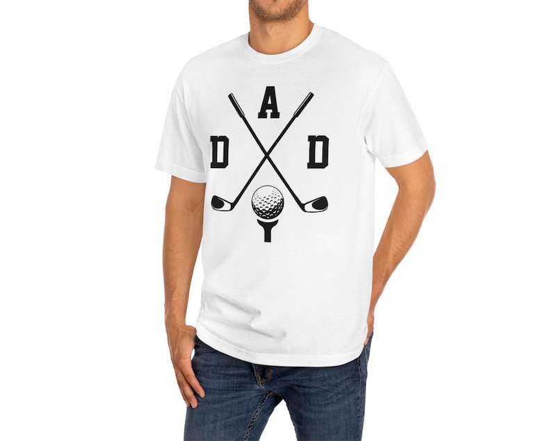 May include: White t-shirt with a black graphic design featuring the word "DAD" with crossed golf clubs, a golf ball, and a tee. The shirt is made of a soft material and is suitable for casual wear.