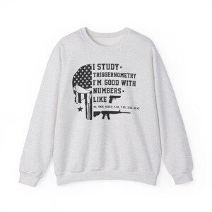 May include: Light gray sweatshirt with a graphic featuring a skull design with an American flag pattern and the text "I STUDY TRIGGERNOMETRY I'M GOOD WITH NUMBERS LIKE" with gun illustrations and ammunition types.