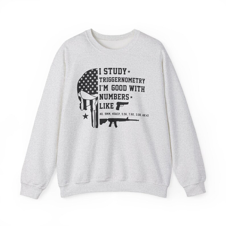 May include: Light gray sweatshirt with a graphic featuring a skull design with an American flag pattern and the text "I STUDY TRIGGERNOMETRY I'M GOOD WITH NUMBERS LIKE" with gun illustrations and ammunition types.