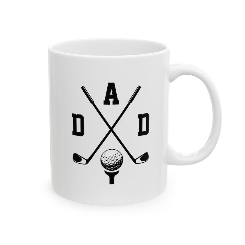 May include: White ceramic mug with a black graphic design. The design features the word "DAD" in bold letters, with crossed golf clubs, a golf ball, and a tee. The mug has a curved handle.