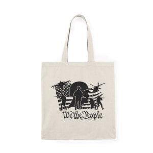 Op de afbeelding: Een beige tote bag met een zwart silhouet van soldaten en een helikopter voor een Amerikaanse vlag. De tekst "We the People" is onder de afbeelding gedrukt.