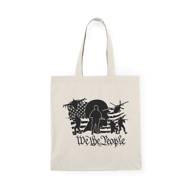 Op de afbeelding: Een beige tote bag met een zwart silhouet van soldaten en een helikopter voor een Amerikaanse vlag. De tekst "We the People" is onder de afbeelding gedrukt.