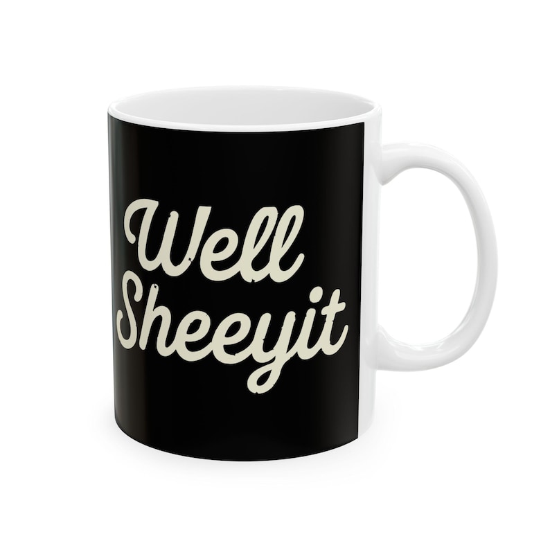 K&ouml;nnte beinhalten: Wei&szlig;e Keramik-Tasse mit schwarzer Au&szlig;enseite. Auf der Tasse steht der Schriftzug "Well Sheeeyit" in kursiver, cremefarbener Schrift. Sie hat einen wei&szlig;en Henkel und Innenraum, f&uuml;r Hei&szlig;- oder Kaltgetr&auml;nke.