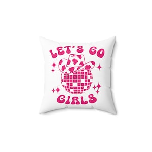 May include: White pillow with pink text that reads "Let's Go Girls" with a pink disco ball and a pink cowboy hat with white spots on top of the disco ball.