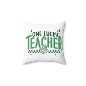Puede incluir: Almohada blanca con texto verde que dice "One Lucky Teacher" con un tr&eacute;bol verde debajo del texto.