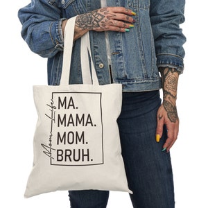 May include: A white canvas tote bag with black text that reads "Ma. Mama. Mom. Bruh." in a box. The bag has white straps.