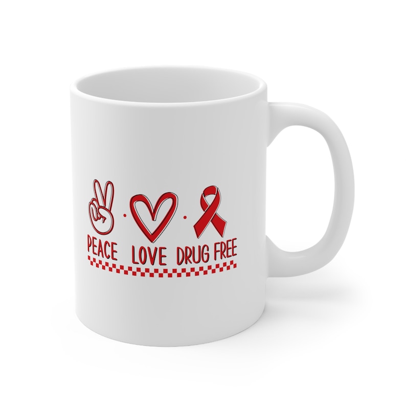 May include: White ceramic coffee mug with a red peace sign, heart, and ribbon with the text "Peace Love Drug Free" and a red and white checkered border.