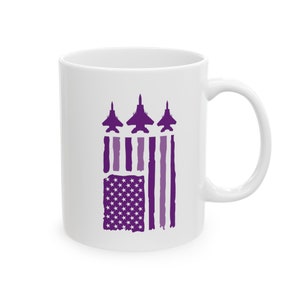 Puede incluir: Taza de cer&aacute;mica blanca con un dise&ntilde;o de bandera estadounidense p&uacute;rpura y tres aviones de combate p&uacute;rpuras volando en formaci&oacute;n sobre la bandera.