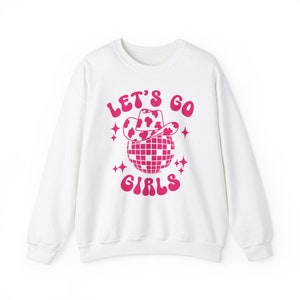 May include: White sweatshirt with a pink graphic of a disco ball wearing a cow print cowboy hat. The text "Let's Go Girls" is written in pink.