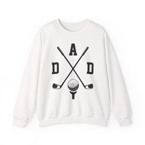 May include: White sweatshirt with a black graphic design featuring the word "DAD" with crossed golf clubs and a golf ball on a tee. The design is centered on the front of the long-sleeved crew neck sweatshirt.
