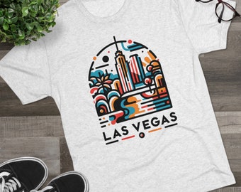 以下が含まれることがあります： 白いTシャツに、カラフルな都市のグラフィックデザインがプリントされており、その下に「LAS VEGAS」の文字が書かれています。