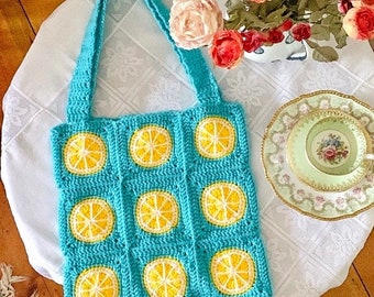 May include: A turquoise crocheted tote bag with yellow lemon designs. The bag has two straps and is made of a soft, textured yarn.
