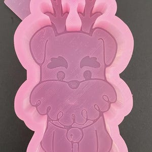 May include: Pink silicone mold for making resin crafts. The mold is shaped like a dog wearing a Christmas light garland and a Santa hat.