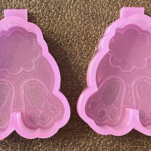 Op de afbeelding: Twee roze siliconen mallen in de vorm van konijnenbillen. Elke mal heeft een reliëfdesign van een konijnenstaart en twee konijnenpootjes.