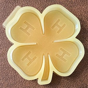 May include: A yellow plastic four-leaf clover mold with the letter "H" embossed on each leaf.