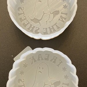 Puede incluir: Dos moldes redondos y transparentes con borde festoneado. Cada molde presenta un gráfico de fantasma con el texto "I'M IN THE SHEETS" en un patrón circular. Los moldes están hechos de un material translúcido.