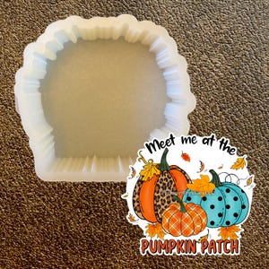 Puede incluir: Un molde de silicona transparente y flexible con borde festoneado, perfecto para manualidades. Una colorida pegatina presenta tres calabazas con varios patrones y el texto "Meet me at the Pumpkin Patch."