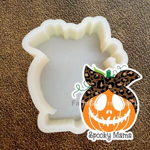 Op de afbeelding: Een witte siliconen mal in de vorm van een pompoen met een gekartelde bovenrand. Een sticker toont een oranje pompoen met een bruin en zwart luipaardprint hoofdband met de tekst FarmGirl Freshies LLC en Spooky Mama.