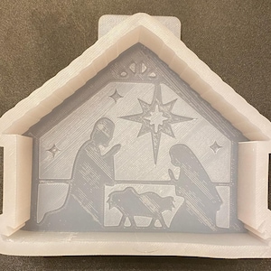 May include: White plastic mold of a nativity scene with a star above the manger. The mold is designed to be used for making resin crafts.