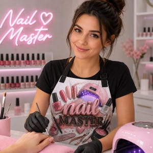 May include: A white apron featuring a graphic print of nail polish bottles, a pink UV nail lamp, nail files, and cuticle nippers. The text "nail MASTER" is printed in large, stylized pink and dark letters across the center of the apron.