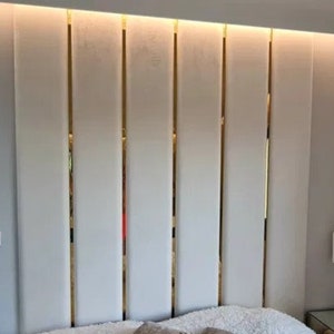 Puede incluir: Una cabecera blanca con tiras doradas verticales. La cabecera está hecha de un material suave y acolchado y tiene un diseño moderno.