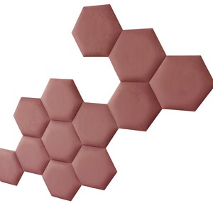 Puede incluir: Un panel de pared hecho de azulejos hexagonales en un color rosa polvoriento. Los azulejos están dispuestos en un patrón escalonado, creando un diseño geométrico.