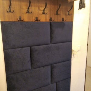 Könnte beinhalten: Eine dunkelblaue gepolsterte Wandverkleidung mit einem Holzregal darüber. Das Regal hat sechs schwarze Metallhaken.