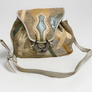 May include: A patchwork backpack with a flap closure and a silver-tone buckle. The bag features a variety of textures and colors, including beige, green, and yellow. It has a long, adjustable strap.