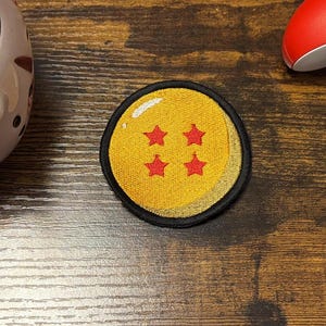 May include: A circular embroidered patch featuring a yellow sphere with four red stars, positioned between a white hockey mask-shaped planter containing a green succulent and a bright red wireless video game controller.