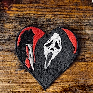 May include: A heart-shaped embroidered patch featuring a white ghost-like mask with black eye and mouth details, a red hood, and a silver knife. The patch is positioned near two spools of Coats & Clark thread and a white hockey mask planter.