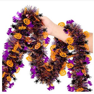 May include: A Halloween tinsel garland featuring a mix of black, orange, and purple metallic strands. The garland is decorated with orange jack-o'-lantern cutouts, purple bat silhouettes, and small black spider shapes attached throughout.