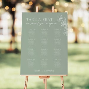 Puede incluir: Un diagrama de asientos de boda verde con texto blanco e ilustraciones florales. El diagrama enumera los nombres de los invitados por número de mesa. El texto en la parte superior dice "TAKE A SEAT we saved you a space". La parte inferior del diagrama dice "MEGAN and ALEXANDER".