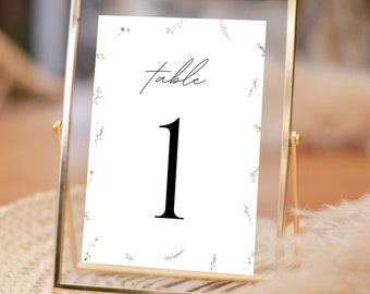 May include: A gold-framed table number card with a white background and a floral pattern. The card says "table 1" in black text.