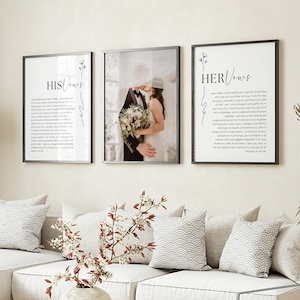 May include: Two framed prints with wedding vows written in black calligraphy on a white background. The prints are hung on a wall above a white couch with gray pillows. The print on the left says "HIS Vows" and the print on the right says "HER Vows".