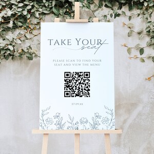 May include: White sign with black text that reads "Take Your Seat" and "Please scan to find your seat and view the menu". A black and white QR code is below the text. The date "07.09.XX" is below the QR code. The sign is decorated with a floral border.